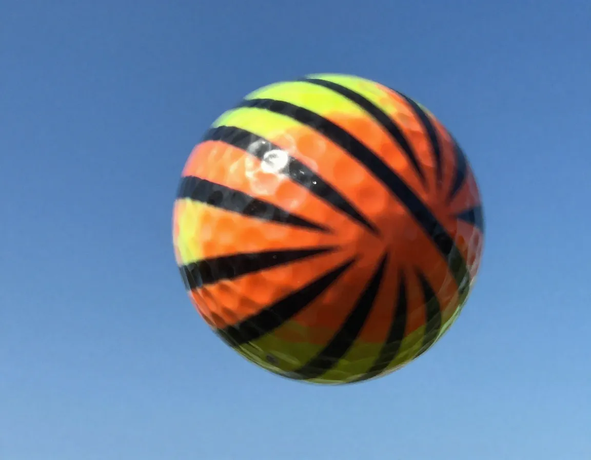 Neon zebra stripe golf ball in mid flight against sky