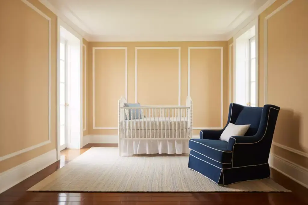 A beige nursery with a white crib, navy blue armchair, and a light rug on a wooden floor.