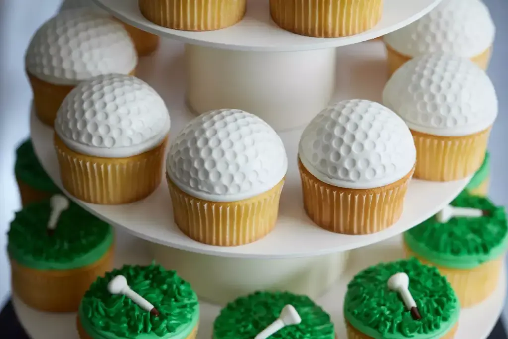 Golf-themed cupcakes on a tiered stand, with white golf ball tops and green grass icing with tees.
