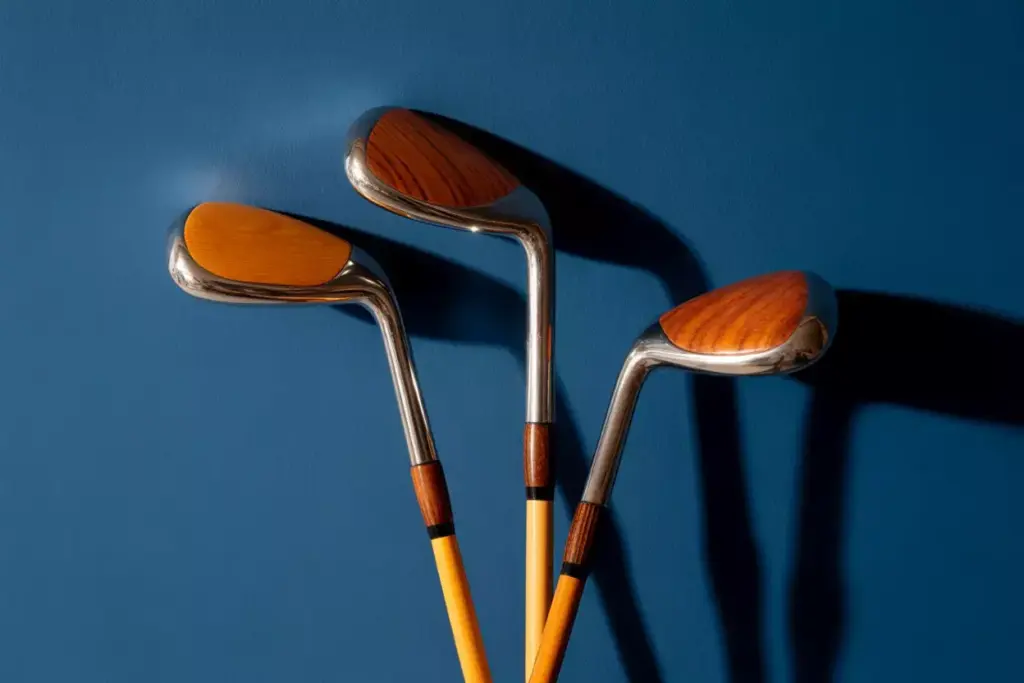 Three wooden golf clubs with metal heads are arranged against a solid blue background.