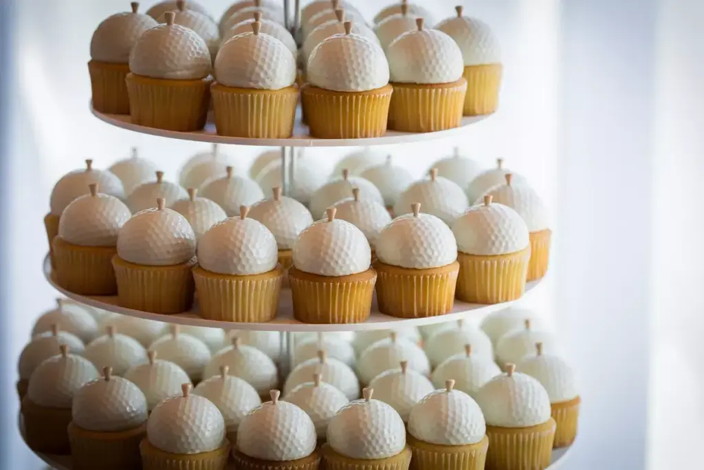 Vanilla cupcakes topped with white golf ball-shaped frosting displayed on a tiered stand.