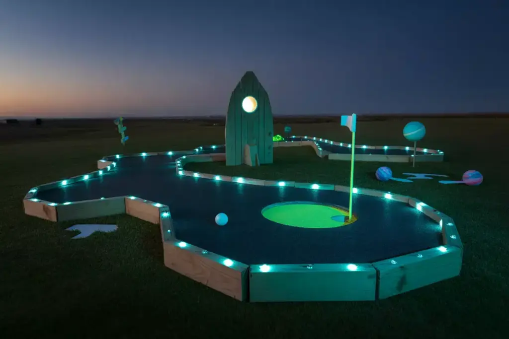A Dark Backyard Mini Golf Hole With Black Turf Glowing Paint And Blue Led Lights At Dusk