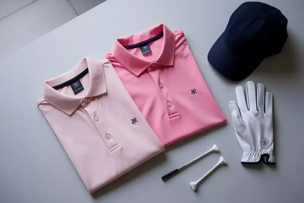 Flat lay of pink golf polos with coordinated accessories on gray