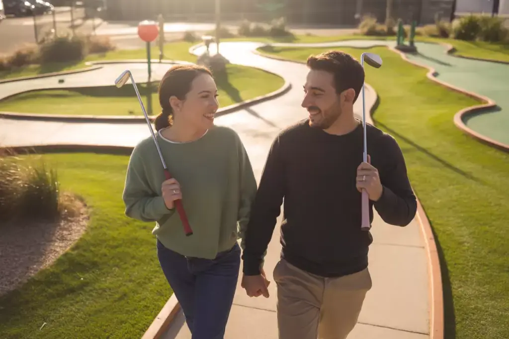 Couple Walking Hand In Hand Putters Shoulders Victory Lap Through Colorful Mini Golf Course