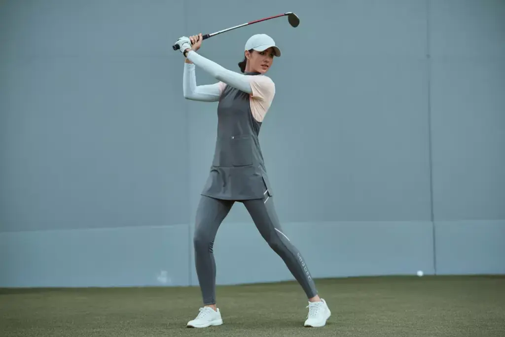 A Woman In High Waisted Leggings And A Tunic Top During A Golf Swing Indoors