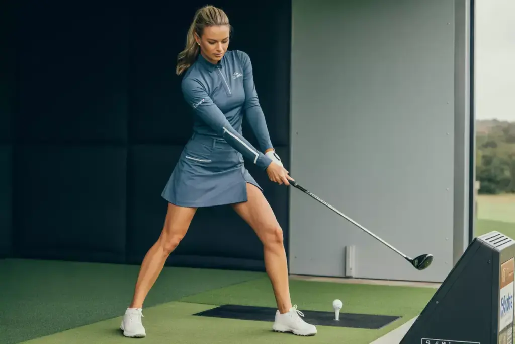 A Woman In A Golf Skort And Long Sleeve Thumbhole Top Preparing For A Shot In A Cool Indoor Facility