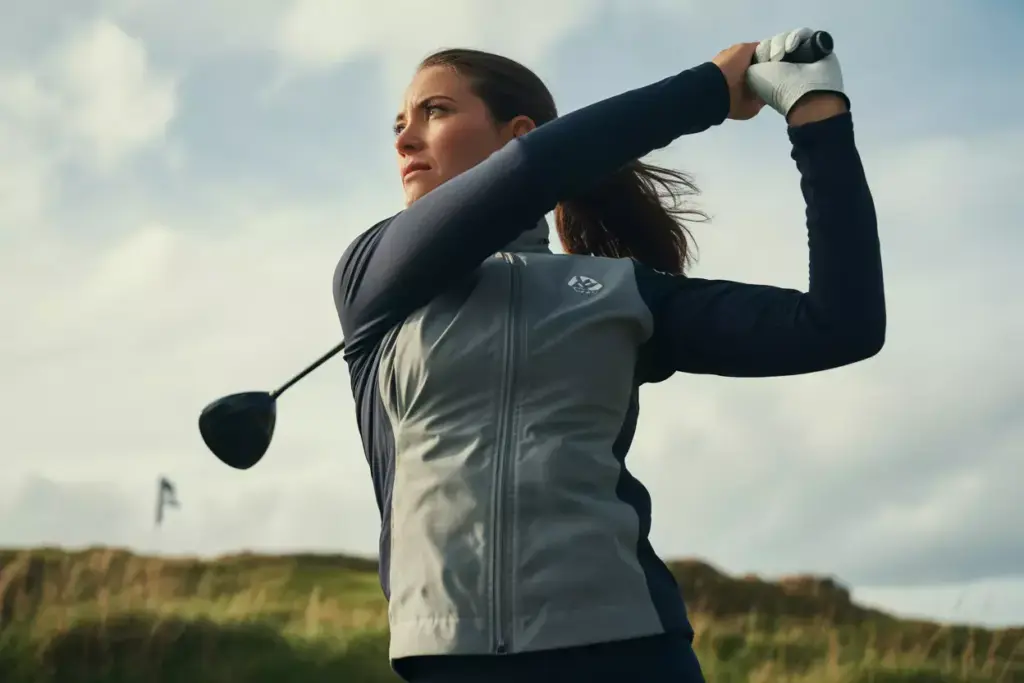 Woman golfer in wind resistant shell executing full backswing action