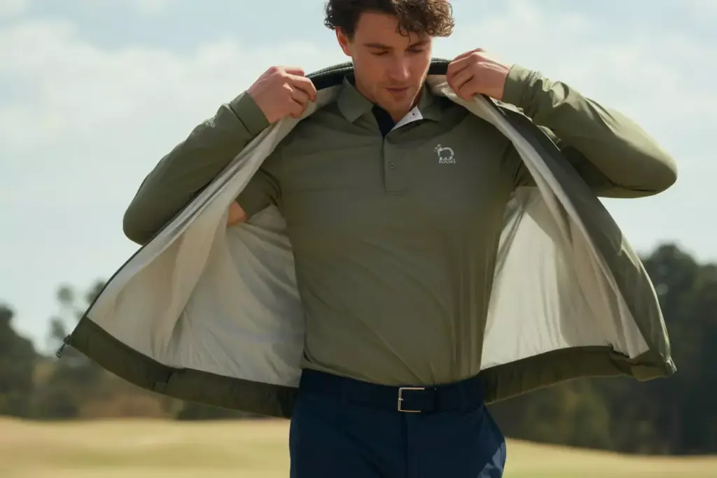Person layering lightweight golf jacket over polo
