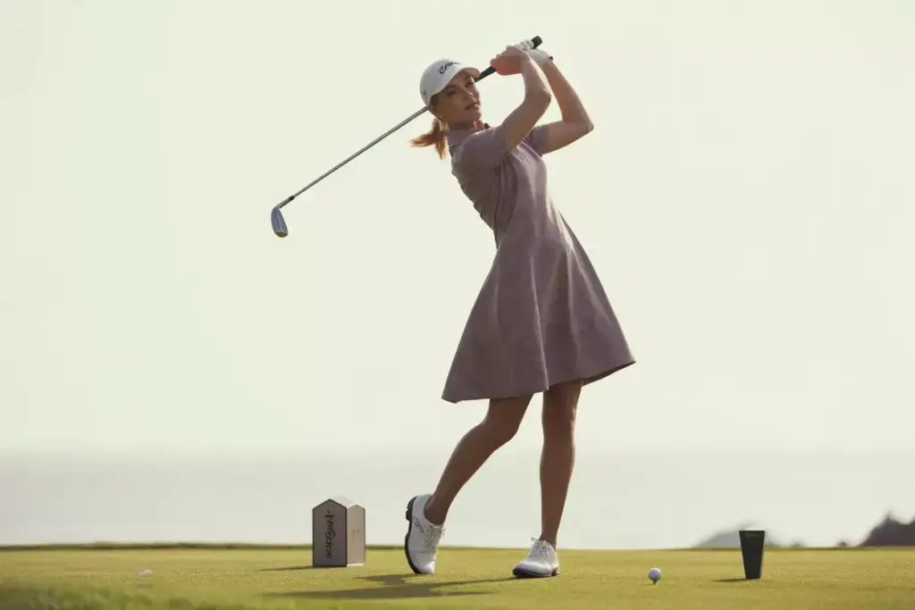 Woman in a line golf dress mid swing on tee box