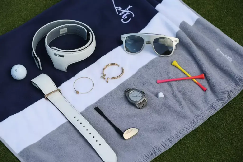 Flat Lay Of Coordinated Golf Accessories Including Belt Sunglasses Watch And Jewelry On Towel