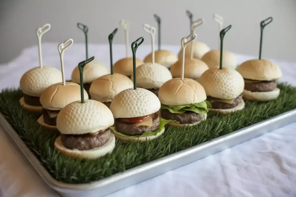 Dimpled Golf Ball Hamburger Buns With Beef Patties Lettuce On Artificial Grass Tray With Golf Tee Picks