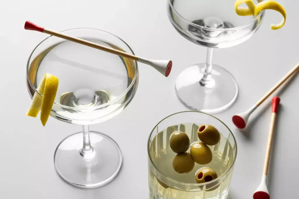 A Martini Glass With A Golf Tee Stirrer And Cocktail On A Light Background